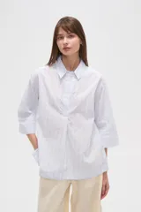 Blusa de algodón a rayas verticales celestes y blancas, holgada, con cuello camisero y mangas 3/4.