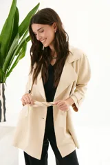 Trench coat color beige de material simil gamuza, con cuello de solapa, cierre frontal con botones y cinturón ajustable en la cintura. Cuenta con bolsillos laterales.