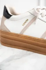 Zapatillas bajas de cuero color blanco y beige, con suela gruesa marrón y cordones blancos.