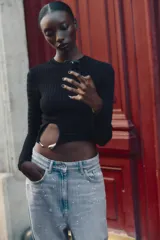 Top corto y ajustado de punto canalé color negro, con cuello redondo, manga larga y detalle de aplique metálico en la parte delantera.