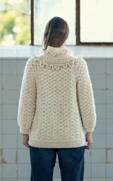 Cardigan tejido a crochet en lana merino color crudo, con volados dobles en hombros y cuello, canesú con tejido abierto y ajuste frontal con cuatro botones de guampa tallados a mano.