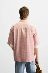 Camisa de corte relajado confeccionada en algodón, con estampado de cuadros pequeños en tonos rosados. Presenta cuello solapa, manga corta y bolsillo plastrón en el pecho con cierre frontal de botones.