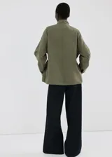 Chaqueta estilo militar verde militar, de diseño oversize, cuello alto, cierre frontal con cremallera y botones ocultos bajo tapeta, bolsillos con solapa y bolsillos de ribete en el pecho.