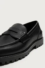 Mocasín de vestir para hombre, confeccionado en cuero sintético negro con acabado liso. Presenta un diseño clásico con detalle de antifaz en el empeine y una suela track robusta y dentada.