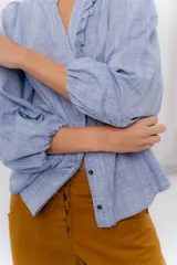Camisa de manga larga color beige con diseño a rayas sutiles, cuello mao con volados y abertura frontal con detalles de volados a un lado.