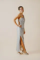 Vestido largo fit al cuerpo color plateado con un solo hombro, diseño fruncido en el lateral, tajo lateral en la falda y abertura en la espalda.