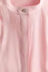 Blusa color rosado con cuello mao y botones ocultos en la parte delantera. Tiene canesú de doble capa con frunces adelante y atrás, mangas cortas abullonadas y puños con abertura y botón.