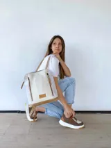 Mochila de cuero color beige y blanco, con detalles laterales texturizados, bolsillos frontales verticales con cierre y asas ajustables.