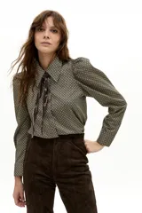 Camisa de manga larga confeccionada en popelina de algodón, con estampado geométrico en tonos verdes y negros. Presenta cuello clásico camisero, hombros ligeramente abullonados y cierre frontal con botones de nácar.