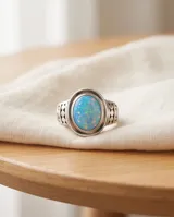 Anillo de plata envejecida con piedra natural ovalada de ópalo en tono celeste y detalles grabados en la banda.