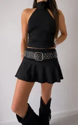 Conjunto de dos piezas compuesto por un top negro sin mangas con cuello alto y una minifalda negra con vuelo. El look se completa con un cinturón ancho negro con tachas metálicas.
