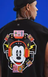 Sudadera sin mangas negra de calce oversize, confeccionada en algodón premium. Presenta un estampado grande en la espalda con la cara de Mickey Mouse usando auriculares, rodeado de elementos gráficos de equipos de música y luces de neón.