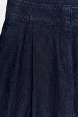 Pantalón tipo culotte de tiro alto confeccionado en denim azul oscuro. Presenta pinzas delanteras, pernera ancha y corta, bolsillos laterales ocultos y cierre frontal con cremallera, botón y ganchos.