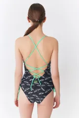 Malla enteriza negra con estampado de hongos blancos, escote en V, tirantes finos color verde neón y laterales ajustables con cordones del mismo color.