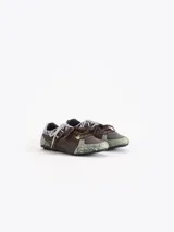 Zapatillas de cuero vacuno en color beige, con recortes de gamuza en la puntera y talón, doble cordón en tonos gris y marrón, hebilla lateral y dije colgante en la cordonera. Suela plana de goma.