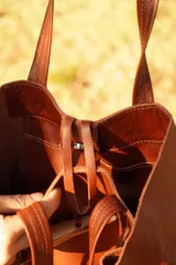 Bolso tipo tote de cuero color marrón, con diseño de flecos laterales y cierre frontal mediante un botón de guampa. Cuenta con doble asa de hombro.