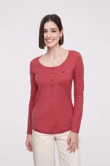 Remera blanca de manga larga, entallada, con cuello redondo y una hilera de botones en el frente. Incluye un pequeño bolsillo decorativo en el pecho.