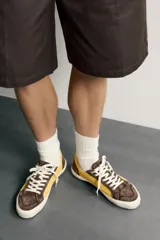 Zapatilla de estilo retro fabricada en una combinación de piel con acabado serraje y algodón, en tonos marrón y amarillo, con suela contrastada.