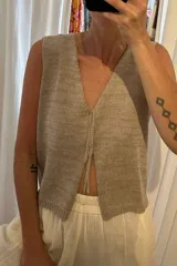 Chaleco de tejido artesanal en color amarillo, con escote en V y cierre frontal mediante lazos anudados. Presenta un diseño sin mangas y corte recto.