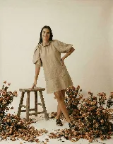 Vestido corto blanco de lino, con cuello redondo con detalle de fruncido y mangas cortas abullonadas. El calce es holgado tipo evasé con un pequeño volante en el ruedo.