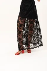 Vestido largo de encaje negro con cuello halter, compuesto por un minivestido base y una sobrefalda transparente de encaje con diseño floral.