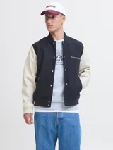 Campera bomber de manga larga y cuello estilo baseball, color azul marino con mangas beige. Tiene cierre de botones, puños acanalados y bolsillos delanteros. Confeccionada en tejido plano con detalle de logo.