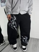 Pantalón de jogging negro de corte holgado, con estampado gráfico estilo tribal en color blanco en la pierna derecha y en el tobillo izquierdo.