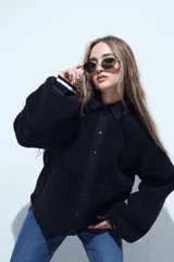 Campera de corderito color marrón oscuro, con cuello camisero y cartera frontal en tela lisa a tono. Presenta cierre mediante botones a presión y mangas largas con puños elásticos.