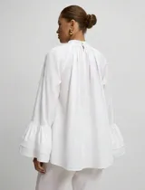 Blusa blanca de algodón con cuello alto fruncido, corte amplio y mangas largas terminadas en doble volado.