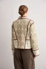 Chaqueta corta capitoneada de color verde claro con estampado tipo paisley y detalles de ribetes en color bordó. Tiene mangas largas, cuello mao y cierre frontal con lazos de atar.