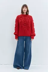 Sweater de punto grueso color rojo, con cuello alto y diseño de relieves tipo pompones en el frente y las mangas. Presenta puños y ruedo acanalados.