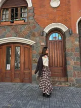 Pollera midi de corte amplio con estampado escocés en tonos marrones. Presenta un diseño distintivo con un detalle de atado en la cintura que simula puños de camisa y cierre frontal con botones.