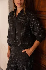 Camisa de manga larga color negro con apliques de strass plateados distribuidos en todo el diseño. Presenta cuello clásico, cierre frontal con botones y puños abotonados.