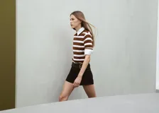 Chaleco de punto a rayas horizontales en tonos marrón y blanco, con cuello camisero blanco y mangas cortas.