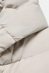 Anorak corto acolchado de Zara, color beige, con cuello subido, capucha, manga larga con puños elásticos y cierre frontal cruzado con botones magnéticos.