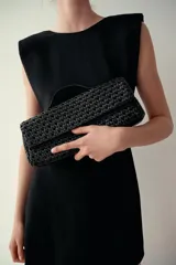 Bolso tipo sobre con diseño trenzado, asa de mano superior y cierre de solapa con imán.