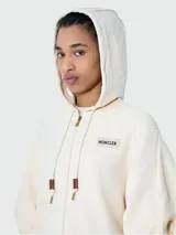 Canguro color crema con capucha, cierre frontal con cremallera dorada, mangas abullonadas 3/4 y logo de la marca en el pecho.