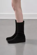 Bota de caña alta confeccionada en gamuza color marrón, con punta cuadrada, taco cuña corrido forrado y cierre lateral.