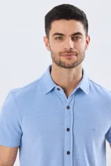 Camisa de piqué lisa color celeste, de manga corta, con cuello camisero y cierre frontal de botones oscuros.