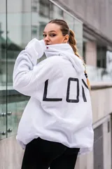 Canguro blanco con capucha y cordones ajustables, puños y cintura acanalados, y estampado negro con letras grandes en la espalda.