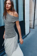 Top gris de escote drapeado, con una manga sisa y una manga corta. Presenta frunces laterales y un bajo asimétrico.