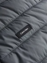 Campera puffer gris con cuello alto y cierre frontal con cremallera. Tiene bolsillos laterales con cremallera y logo de Calvin Klein en el pecho y en la manga.