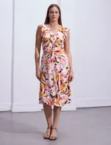 Vestido camisero midi estampado con flores en tonos rosa, naranja y marrón sobre fondo blanco. Tiene escote en V, abertura frontal con botones, mangas cortas con volados y lazo de ajuste en la cintura.