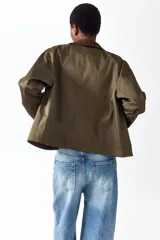 Campera de sarga color verde militar, con cuello camisero de pana marrón oscuro, cierre frontal con solapa y botones a presión metálicos, bolsillos frontales grandes con solapa y mangas raglán.