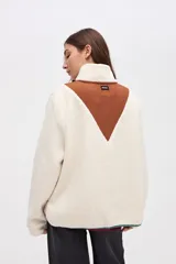 Buzo de sherpa color marrón con diseño de medio cierre frontal. Presenta un panel superior en forma de V en color beige y detalles de vivos en color fucsia en el cierre, cuello y bolsillos laterales. Cuenta con cuello alto y bolsillos frontales.