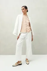 Camisa color marrón claro con cuello mao, mangas 3/4 abullonadas y cierre frontal con botones. Presenta pequeños pliegues en los hombros y detalle calado sutil.