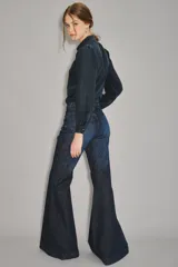 Jean de corte acampanado estilo setentero, confeccionado en denim azul oscuro. Presenta una cintura con detalle de trenzado integrado y un calce ajustado en la parte superior que se ensancha desde la rodilla hacia abajo.