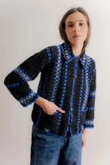Saco tejido a mano en crochet con diseño de rayas verticales, manga larga y cuello camisero. Presenta cierre frontal con botones y bolsillos delanteros aplicados.