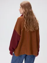 Pullover de tejido acanalado grueso con diseño bicolor en tonos marrón y bordó. Presenta cuello alto con cierre frontal, mangas largas y corte holgado.