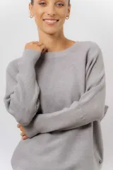 Buzo tejido de punto en color beige, con cuello redondo, mangas largas y silueta relajada con dobladillo irregular, siendo más largo en la parte trasera.